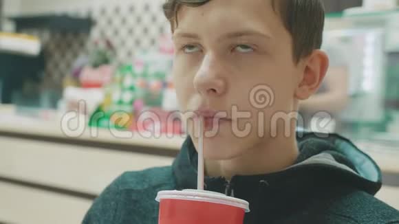 十几岁的孩子喝着一杯可乐从一个管子里拿着一杯口渴的纸咖啡馆里的男孩快餐那个男孩喝了视频的预览图