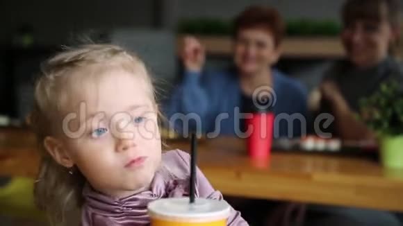 这个女孩在他母亲和祖母的背景下喝果汁视频的预览图