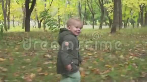 两岁的男孩在秋天的森林里奔跑公园视频的预览图