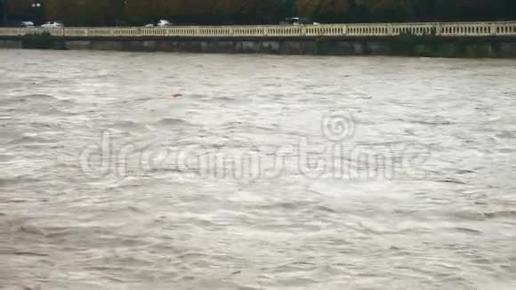 灰色的不透明河水在市中心的一座围栏大坝的河床中迅速流动下雨的天气洪水泛滥视频的预览图