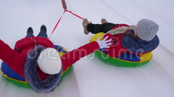 穿红色夹克的孩子们在冬天骑着充气雪管穿过雪地扮演超级英雄快乐的女孩视频的预览图