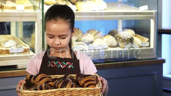 可爱的小女孩穿着围裙在面包店工作手里拿着一个篮子和糕点视频的预览图