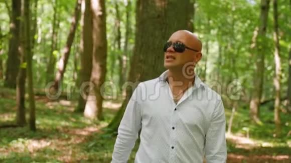一个戴墨镜的秃子唱歌穿过树林绿树夏天大自然中弹视频的预览图