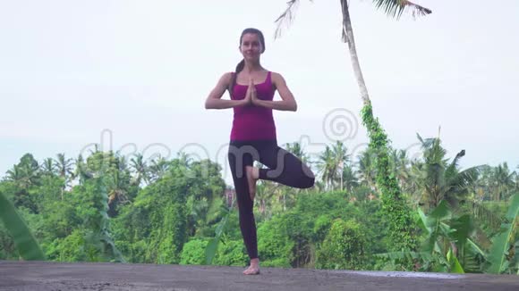在巴厘岛练习瑜伽树姿的年轻女子视频的预览图