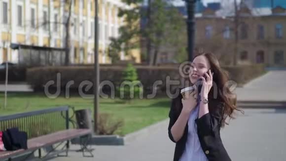 美丽的黑发女人走在城市的街道上用手机说话带着咖啡走的女人视频的预览图