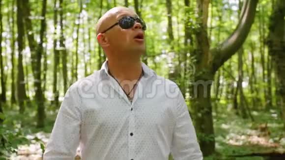 一个戴墨镜的秃子唱歌穿过树林绿树夏天大自然中弹视频的预览图