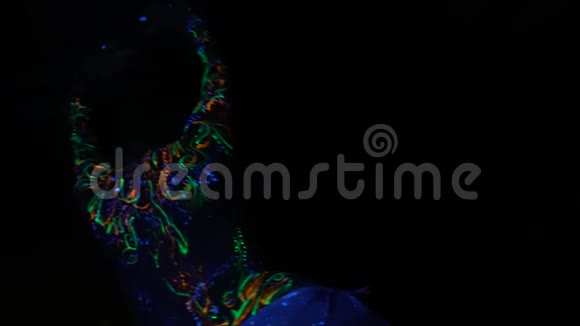 一个神秘的女孩穿着五颜六色的图案在黑暗中发光慢慢地跳舞慢动作视频的预览图