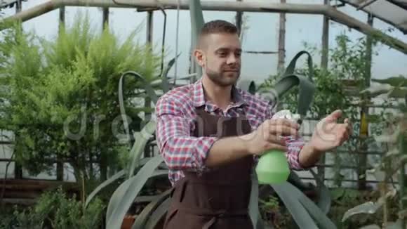 在温室里用花园喷雾器浇灌植物和花朵的迷人的园丁的多利照片视频的预览图