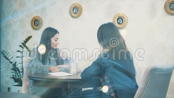 坐在咖啡馆里的漂亮年轻女人一个穿着休闲服装的白种人女孩从窗户里走出来的美丽而温暖的镜头视频的预览图