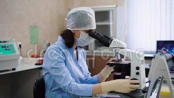 专业女性实验室助理穿蓝色实验室外套防护面罩帽子和手套坐在柜子里视频的预览图