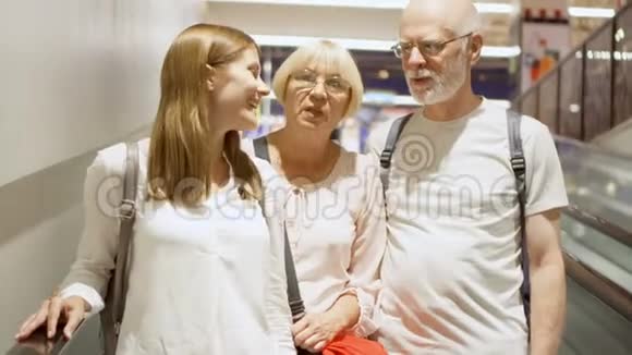 购物中心自动扶梯上的幸福家庭年长夫妇和他们的女儿谈笑风生视频的预览图