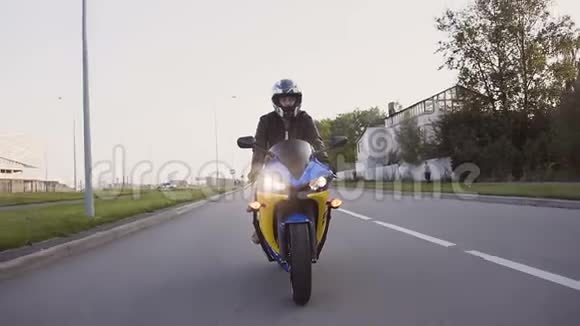一个穿着皮夹克和头盔的年轻骑摩托车沿着城市的高速公路特写视频的预览图