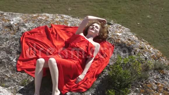 一个穿着红色裙子的奢华女人躺在岩石上视频的预览图