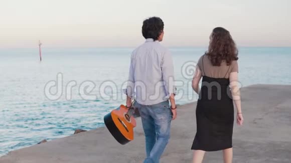 美丽的音乐家夫妇沿着海边的码头散步视频的预览图