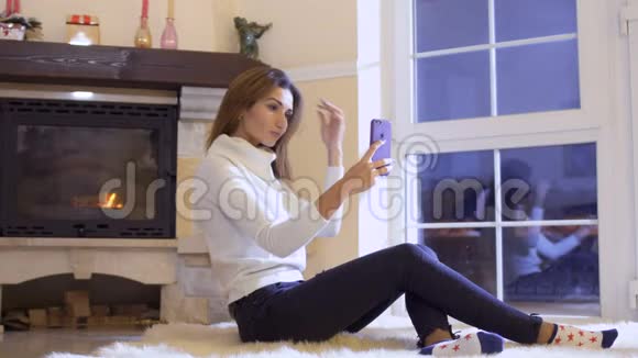 漂亮的女孩坐在地板上在智能手机上自拍视频的预览图