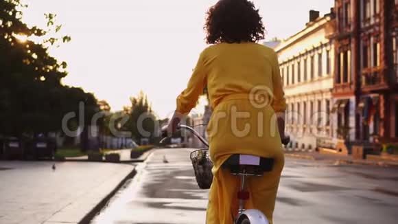 在城市里一个穿着黄色长裙骑着一辆自行车篮子和鲜花面目全非的女人的后景视频的预览图