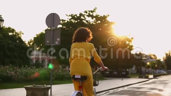 黎明时分一位身着黄色长裙的女子骑着一辆城市自行车在市中心的后景视频的预览图