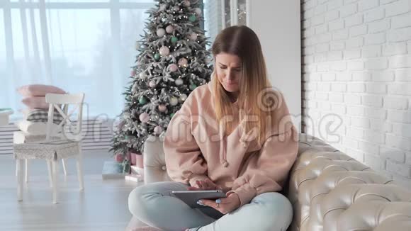 快乐的年轻女性坐在沙发上在平板电脑上浏览互联网在线支付在线购买使用方便视频的预览图