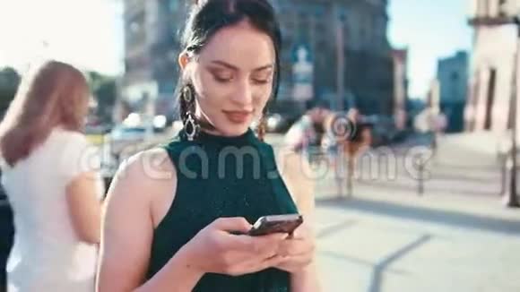 漂亮的黑发女孩梦游地看着她的手机屏幕迷人的微笑和短信而站在里面视频的预览图