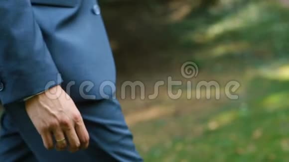 这位穿着蓝色西装的无名新郎正在公园里散步时把手放在口袋里特写侧视视频的预览图
