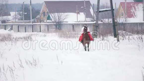 穿着红色连衣裙的漂亮黑发少女在冬天的雪地里飞快地骑在马背上视频的预览图