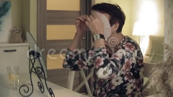 一位老妇人照镜子从脸上摘下一个化妆组织面具面部护理整形手术和胶原蛋白视频的预览图