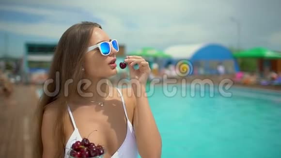 夏天美丽的年轻女子比基尼女孩在热带游泳池放松女人吃樱桃概念视频的预览图