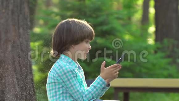 孩子们在绿色公园夏天户外玩手机孩子用无线网络可爱的快乐男孩在网上写短信视频的预览图