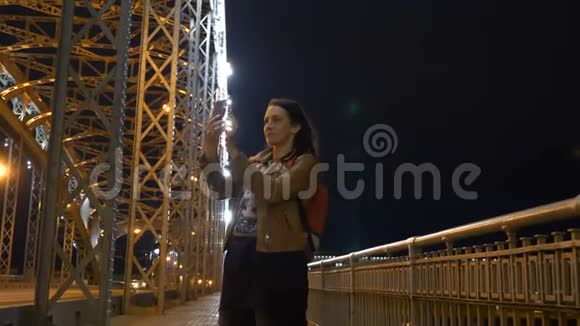 在圣彼得堡晚上在桥上用手机自拍的女人视频的预览图