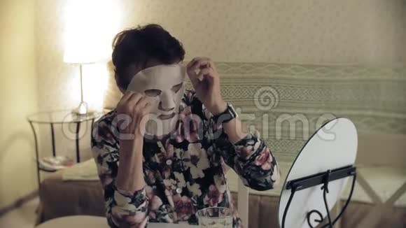 一位老妇人照镜子从脸上摘下一个化妆组织面具面部护理整形手术和胶原蛋白视频的预览图