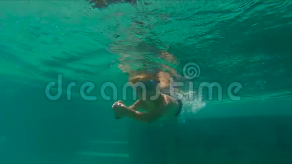 一个可爱的小男孩手里拿着两颗在水下的鹅卵石潜入游泳池动作缓慢视频的预览图