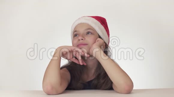 美丽的快乐女孩少年戴着圣诞老人的帽子在白色背景的股票视频中快乐地做梦和欢笑视频的预览图