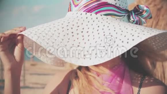 在海滩和大海的背景下一个年轻的女人在风中缓慢地拿着她的帽子视频的预览图