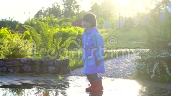 快乐可爱的小男孩喜欢跑步玩得开心穿着雨衣和橡胶靴在水坑里跳笑笑视频的预览图