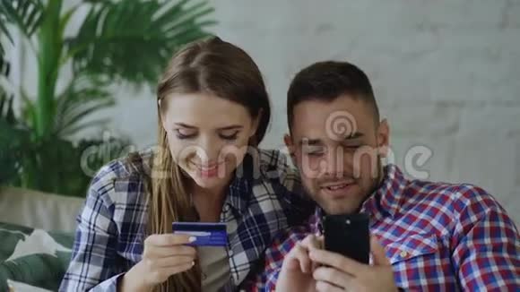 在互联网上购买智能手机和信用卡的新婚夫妇坐在客厅的沙发上视频的预览图