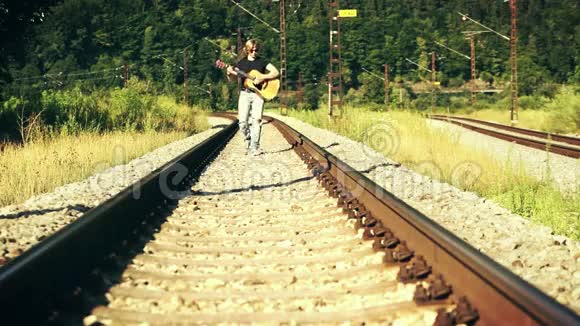 很酷的左撇子长头发的家伙拿着吉他沿着铁路走视频的预览图
