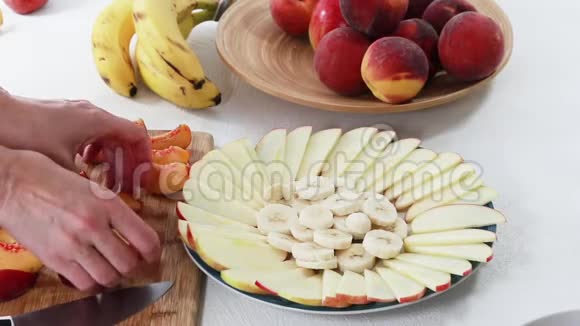 新鲜水果盘苹果桃子和香蕉片放在盘子里贴在白色背景上女人的手视频的预览图