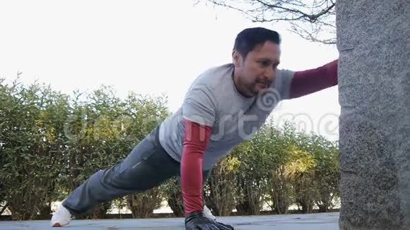 与户外私人教练一起健身健身男子在公园里做手臂俯卧撑作为锻炼常规的一部分视频的预览图