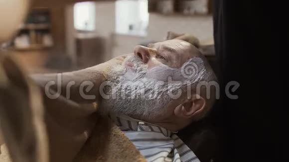 理发师用热毛巾遮住成熟男人的脸然后刮胡子视频的预览图