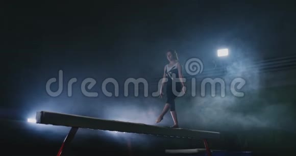 女孩是一名职业运动员在运动中背光和慢动作的横梁上表演体操杂技视频的预览图