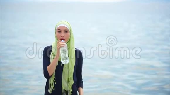 一位戴头巾的年轻女士在户外热天从瓶子里喝矿泉水视频的预览图