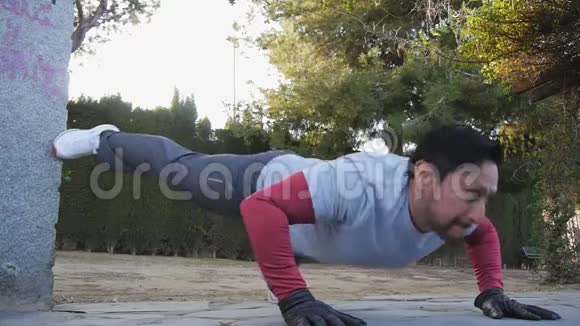 与户外私人教练一起健身健身男子在公园里做抬腿俯卧撑作为锻炼常规的一部分视频的预览图