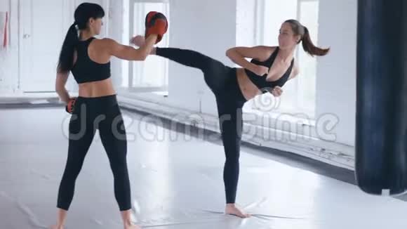 运动女性训练她的踢腿在她的教练持有的一个冲孔袋跆拳道或跆拳道的训练二视频的预览图
