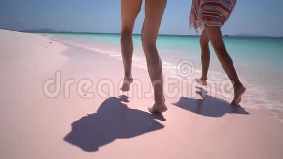 两个美丽的朋友在海滩上奔跑沙滩上靠近水边海浪拍打着美丽的晒黑的腿视频的预览图