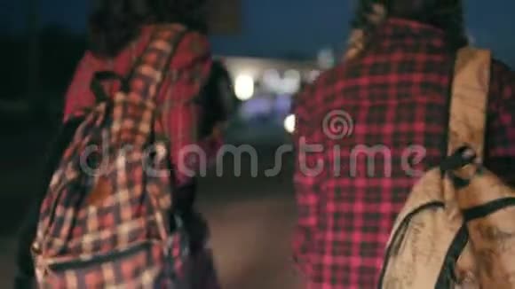 两个年轻的女搭便车者站在一旁手里拿着背包要求在晚上阻止过往的汽车视频的预览图
