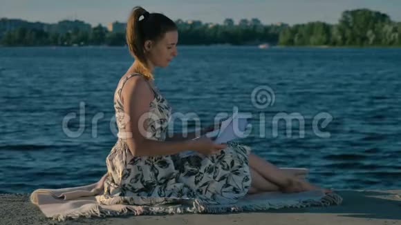 年轻女子在河边的毯子上放松翻阅报纸视频的预览图