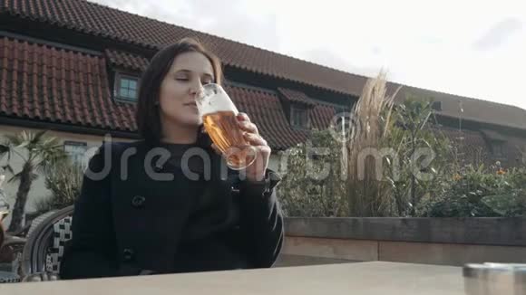 年轻女子在街头餐厅喝啤酒在阳光明媚的日子里女孩在街上的咖啡馆里喝啤酒视频的预览图