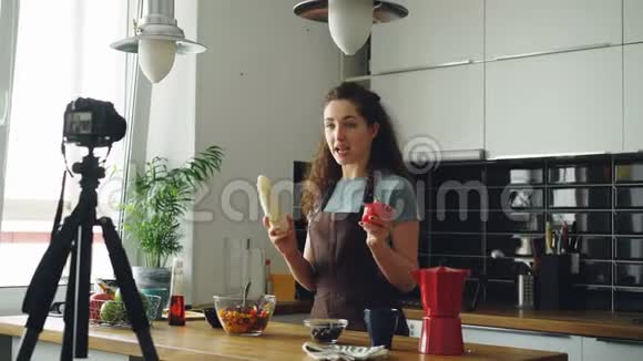 有魅力的女孩在家里的厨房里用数码相机录制关于健康烹饪的视频食物vlog记录和记录视频的预览图