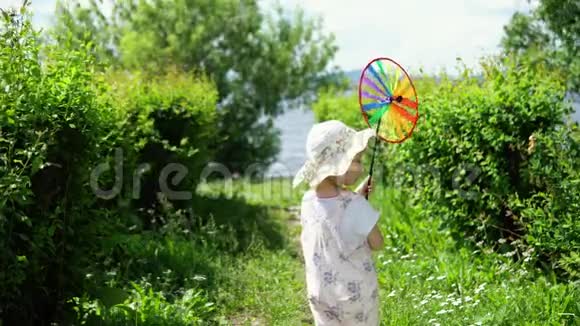 一个小可爱的女孩在温暖的一天在花园里玩一个五颜六色的风车视频的预览图