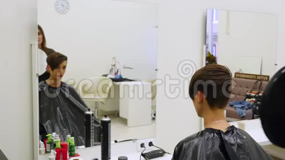专业的理发师用镜子向英俊的满意的女性客户展示理发的背面视频的预览图